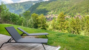 Una terraza de madera con dos sillones de descanso que ofrece vistas a un paisaje montañoso con un pueblo abajo.
