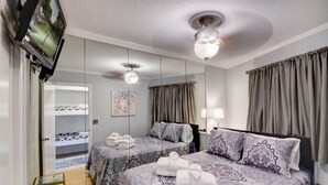 Ein Hotelzimmer mit einem großen Spiegel, zwei Betten mit gemusterten Betttextilien, einem Deckenventilator und einem an der Wand montierten Fernseher.