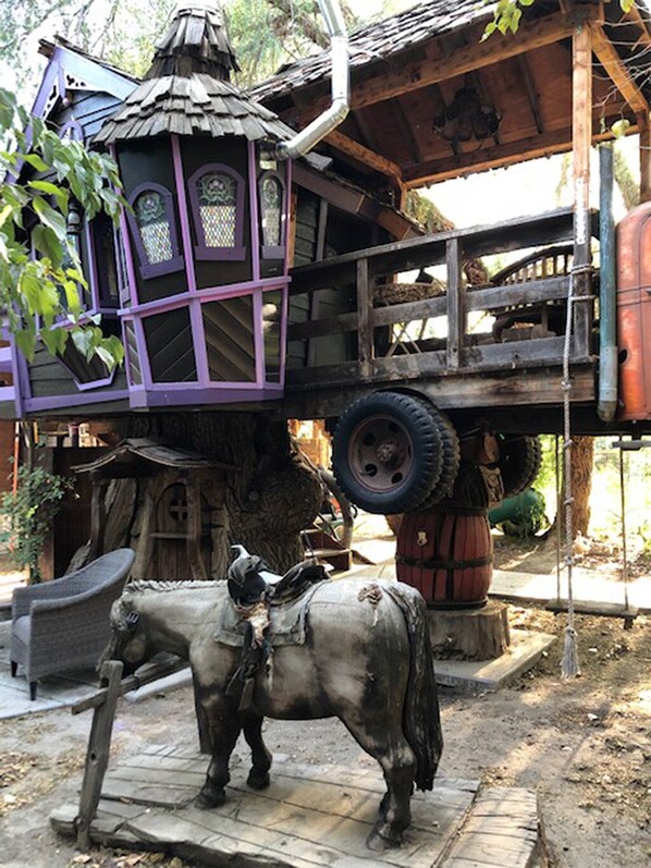 A rustic wooden structure with a thatched roof, a small balcony, and a large tire mounted on a wooden stand.