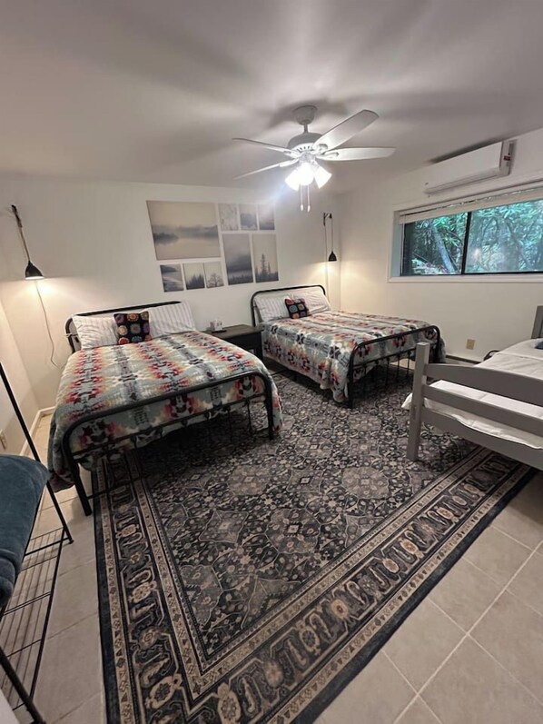 A bedroom with two beds, a ceiling fan, a window with a view of trees, and a patterned rug.