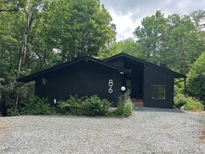 A modern black building with a gravel driveway and lush greenery.