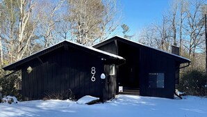 A cabin with a dark exterior, a chimney, and a snow-covered ground. - Modern Mountain Cabin Close to Skiing w/firepit (Newland)