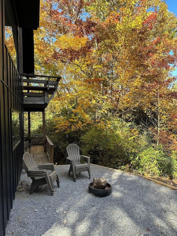 A covered outdoor seating area with two Adirondack chairs and a fire pit.