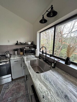 A modern kitchen with a large window, stainless steel appliances, and a marble countertop.