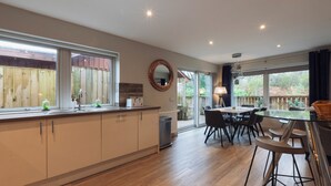 A modern kitchen with a large island, wooden flooring, and a dining area with a glass table and chairs. - Hot tub lodge with stunning view (Taynuilt)