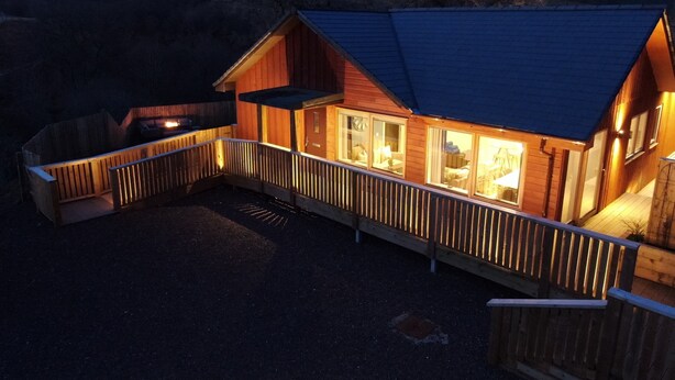 A wooden cabin with a covered deck and a fireplace. - Hot tub lodge with stunning view (Taynuilt)