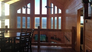 A wooden cabin with a dining area, large windows, and a view of the mountains. - 360 Mountain Top Views! Private Pool, Gated, Theatre, Pinball, Outdoor Kitchen! (Sevierville)