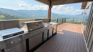 An outdoor kitchen with a grill and oven, a wooden deck, and a view of mountains. - 360 Mountain Top Views! Private Pool, Gated, Theatre, Pinball, Outdoor Kitchen! (Sevierville)