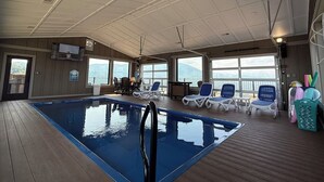 An indoor swimming pool with clear views of the ocean, surrounded by lounge chairs and a wooden deck. - 360 Mountain Top Views! Private Pool, Gated, Theatre, Pinball, Outdoor Kitchen! (Sevierville)