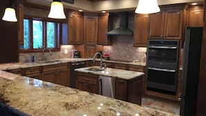 A kitchen with wooden cabinets, granite countertops, stainless steel appliances, and pendant lighting. - 360 Mountain Top Views! Private Pool, Gated, Theatre, Pinball, Outdoor Kitchen! (Sevierville)