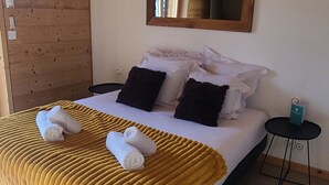 A neatly made bed with a yellow blanket, white pillows, and a wooden headboard. There is a small bedside table with a green item on it.