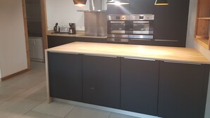 A modern kitchen with dark cabinetry, stainless steel appliances, and a wooden countertop.