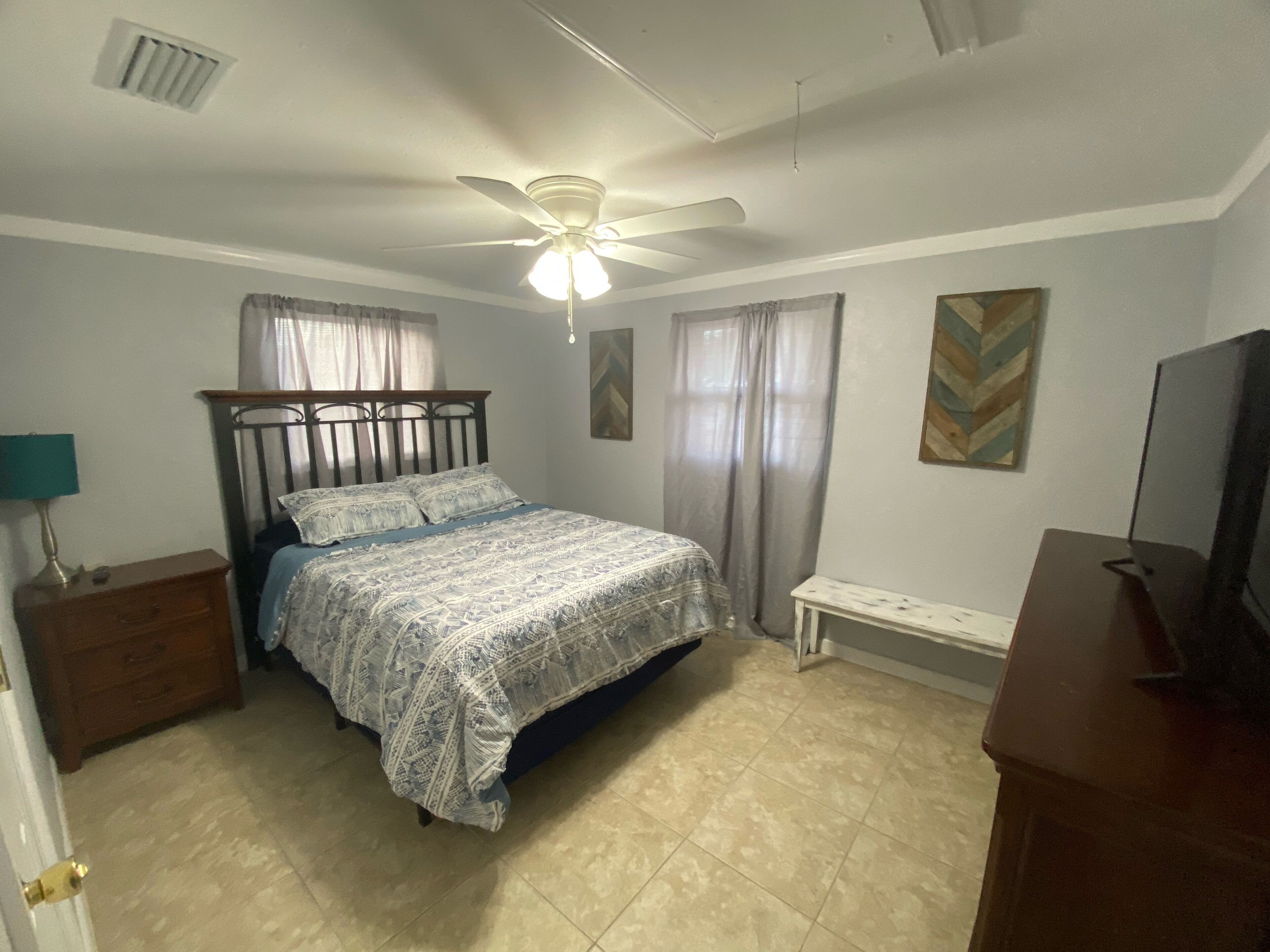 A bedroom with a bed, a ceiling fan, a nightstand, a dresser, and a television.