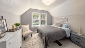 Een slaapkamer met een bed, een dressoir, een stoel en een raam.