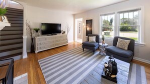 Een moderne woonkamer met een flatscreen televisie, een witte console, twee grijze banken en een gestreept vloerkleed.