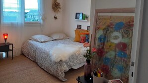 A bedroom with a bed, a bedside lamp, a wall-mounted TV, and a window with curtains. - Cosy and bright 1-3 person apartment (caen)
