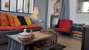 A living room with a grey sofa, colorful cushions, a small coffee table with a woven basket, a red armchair, and a blue side table with a lamp. - Cosy and bright 1-3 person apartment (caen)