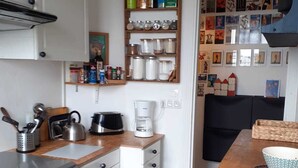 A compact kitchen with a stove, oven, coffee maker, and a wooden shelf with jars. - Cosy and bright 1-3 person apartment (caen)