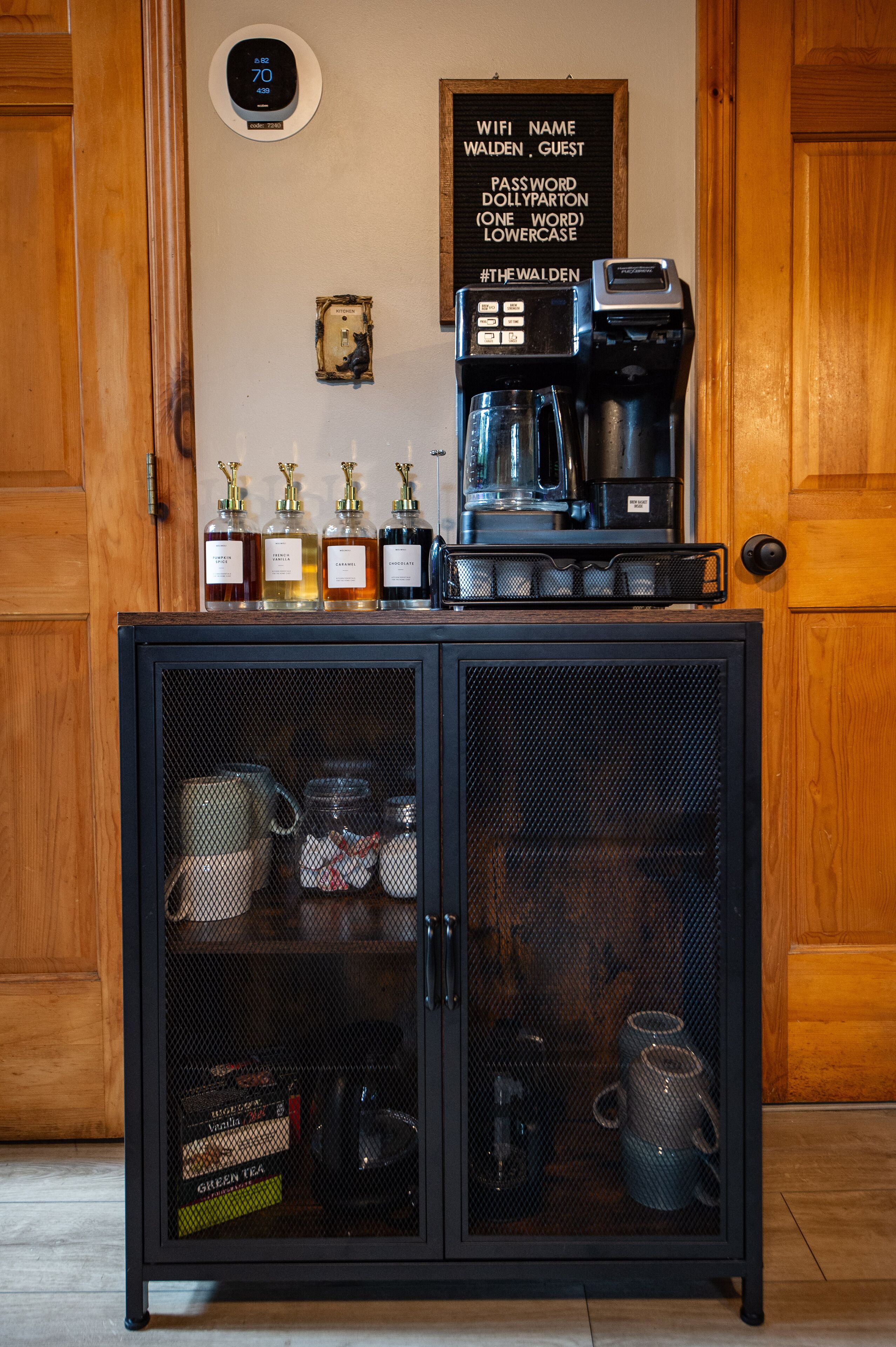 A coffee station with a coffee machine, a sign with Wi-Fi details, and a cabinet with kitchenware.
