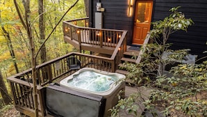 Un bain à remous sur une terrasse en bois, avec une rambarde en bois et une porte donnant sur un chalet.
