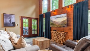 Un salon chaleureux avec un mur en bois, une grande fenêtre avec des rideaux, un canapé, une table basse et un tableau.
