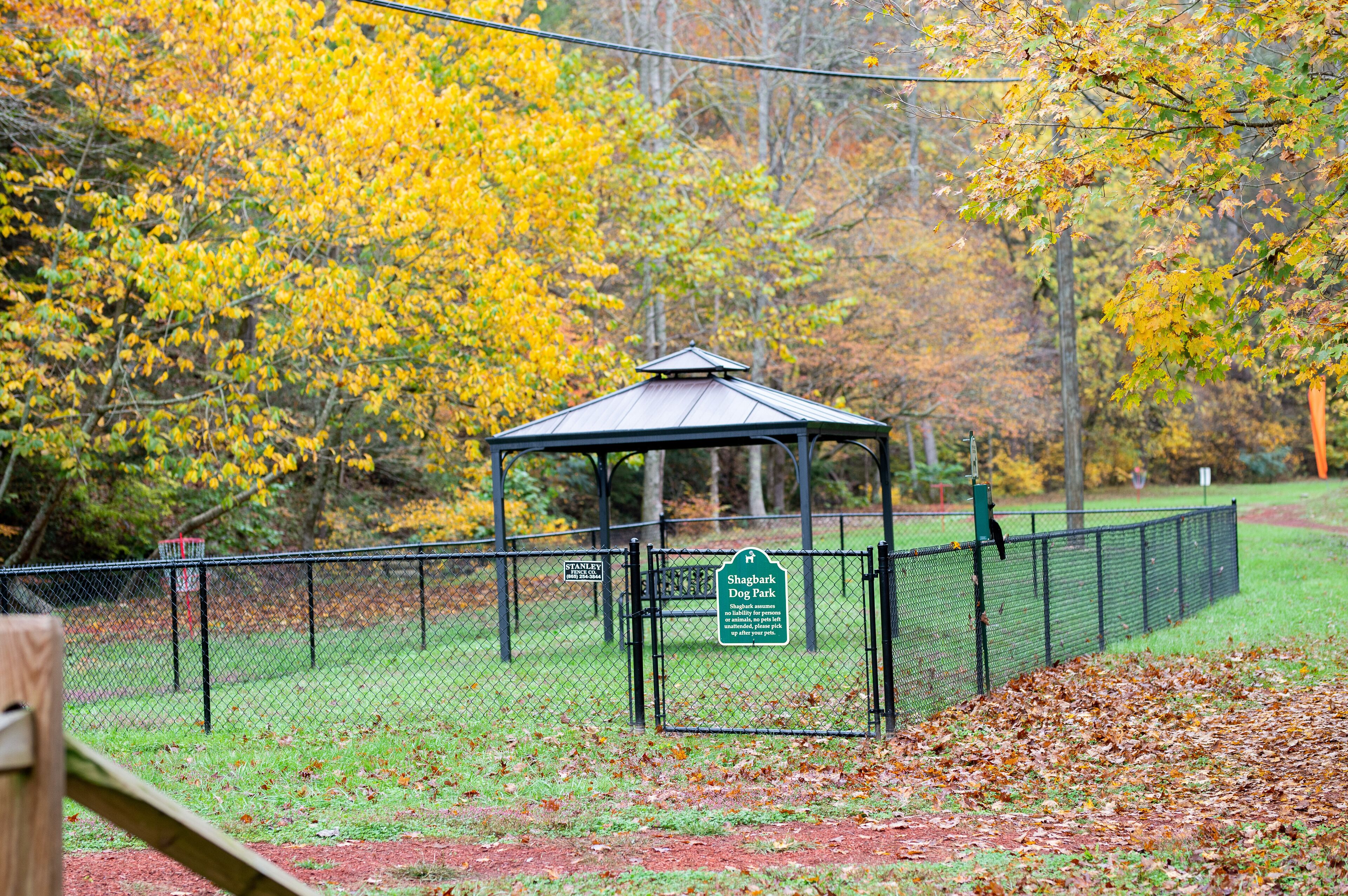 A gazebo in a park with a fenced area and a sign indicating it is a dog park.