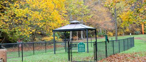 A gazebo in a park with a fenced area and a sign indicating it is a dog park.