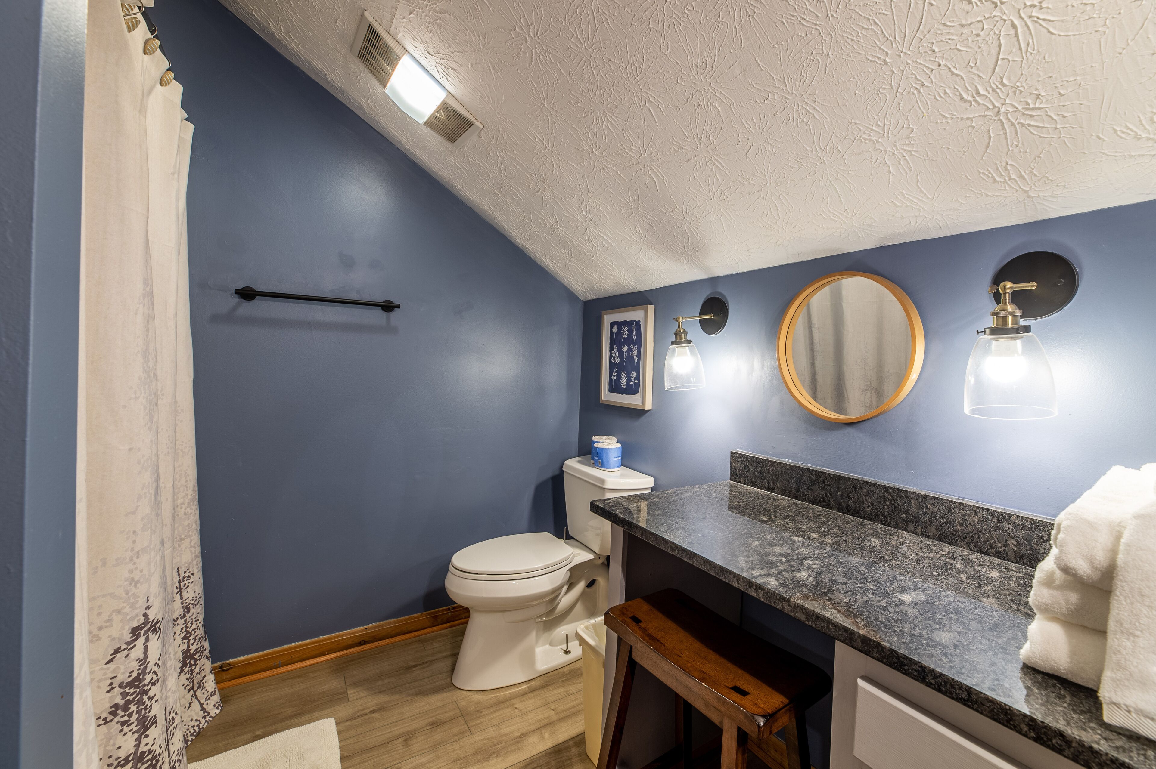 A bathroom with a blue wall, white toilet, and granite countertop.