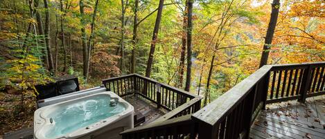 A hot tub on a wooden deck surrounded by autumn foliage.