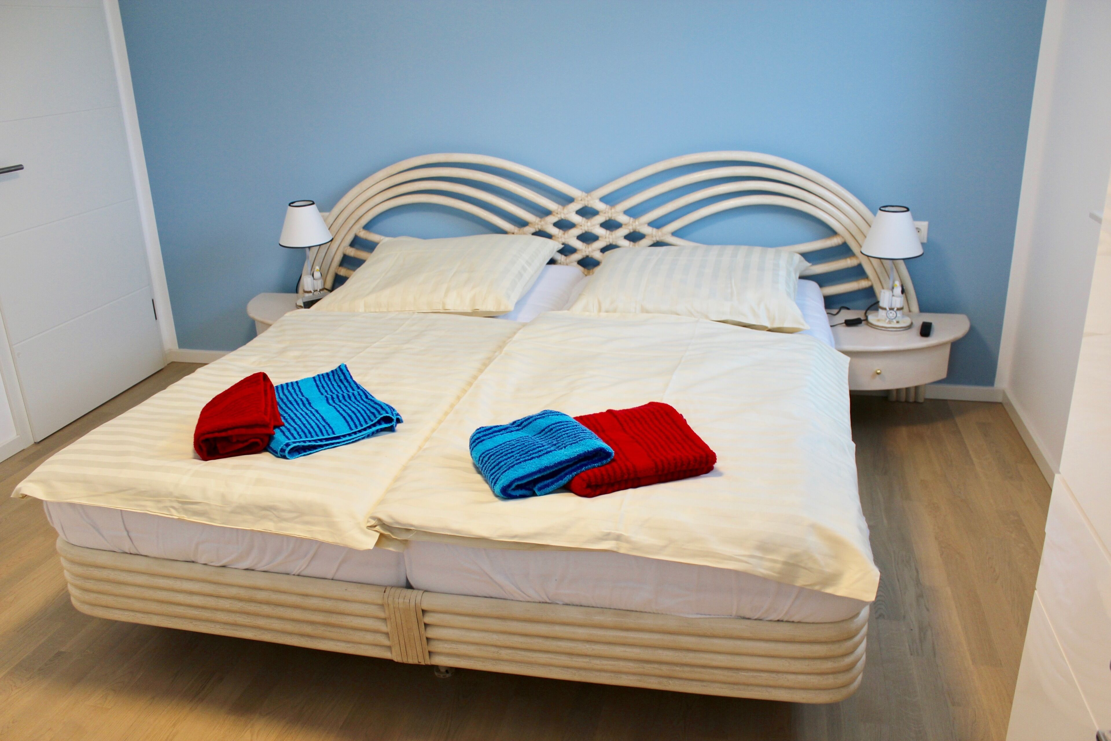 A double bed with white linens, two nightstands with lamps, and a blue wall.