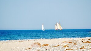 Ein Strand mit zwei Segelbooten auf dem Wasser und Kieselsteinen im Vordergrund.