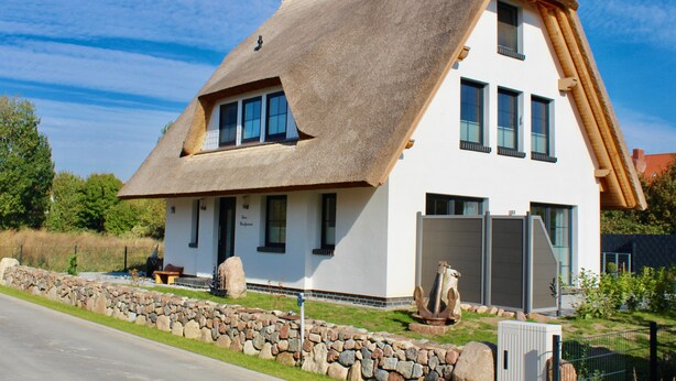 Ein modernes Haus mit steil geneigtem Strohdach, großen Fenstern und einem Steinfundament.