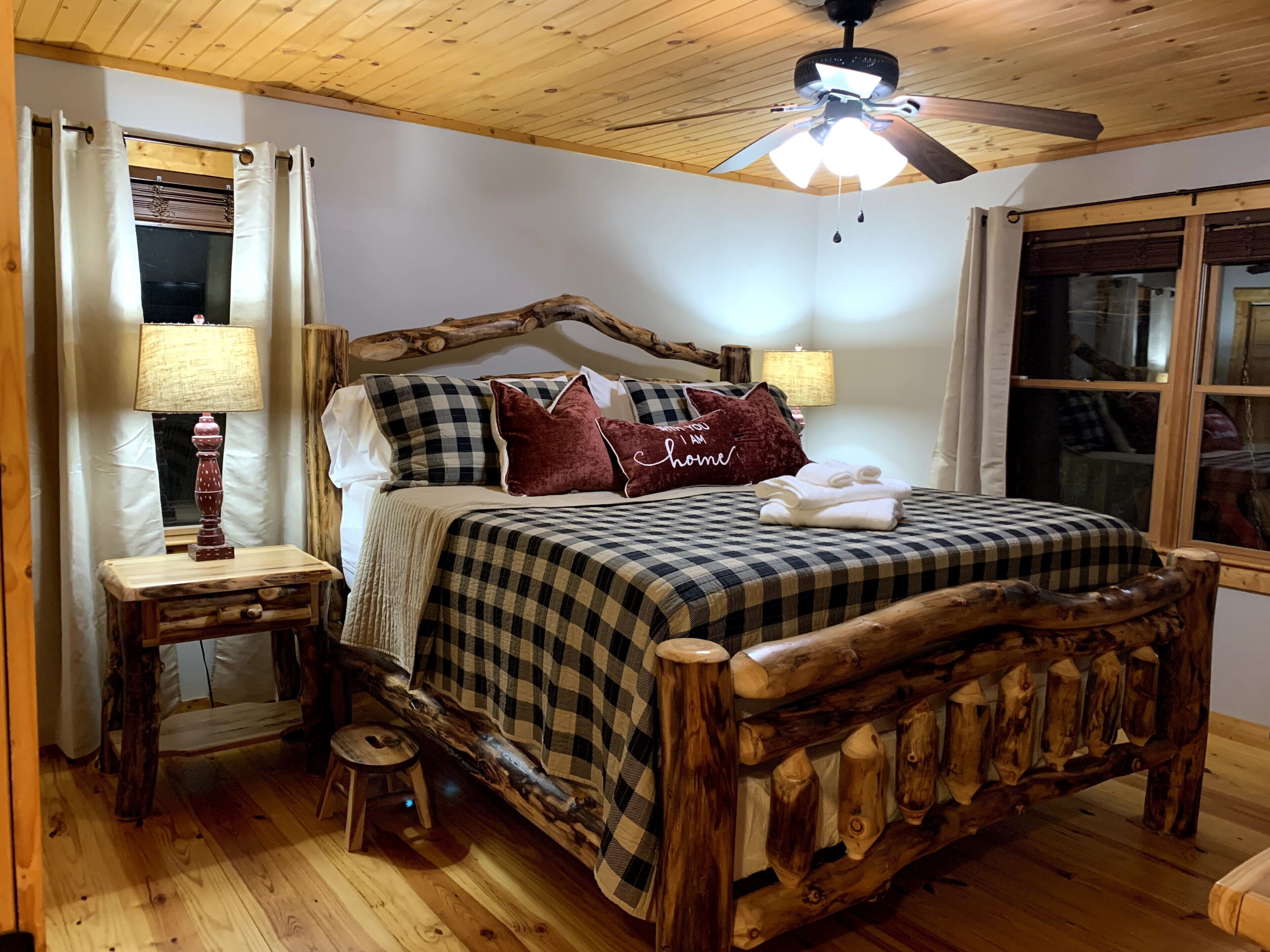 A wooden bed with a checkered bedspread and pillows, a wooden nightstand with a lamp, and a ceiling fan.