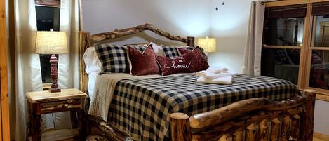 A wooden bed with a checkered bedspread and pillows, a wooden nightstand with a lamp, and a ceiling fan.