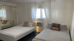 Une chambre avec deux lits simples, une table de chevet avec une lampe, une fenêtre avec des rideaux et un luminaire au plafond.