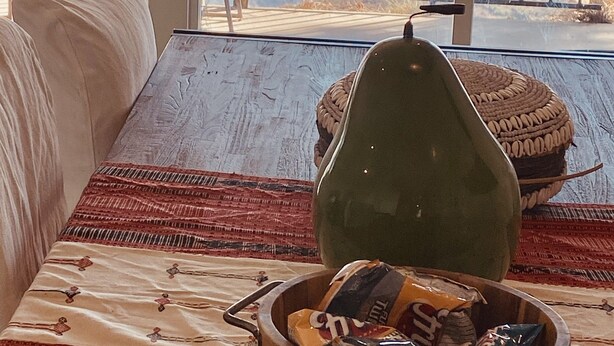 Une pièce avec vue sur la mer, une table en bois sur laquelle se trouve un bol rempli de collations, un panier en osier et une chaise.