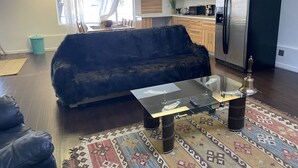 Un salon moderne avec un canapé noir, une table basse en verre et un tapis à motifs.