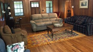 Ein gemütliches Wohnzimmer mit Holzwänden, einem beigefarbenen Sofa, einem karierten Sofa und einem Couchtisch.