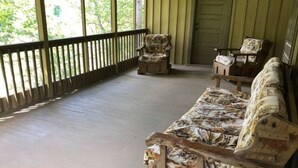 Eine überdachte Veranda mit Holzboden, zwei Polsterstühle und einer Tür.