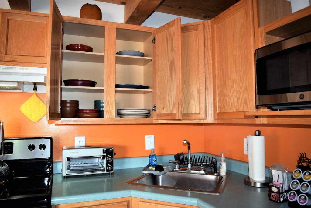 Une cuisine avec des meubles de rangement en bois, une cuisinière noire, un grille-pain blanc, un évier et un four à micro-ondes.