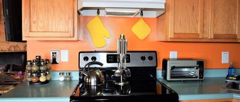 A kitchen with wooden cabinets, a stove, a toaster oven, and a kettle.