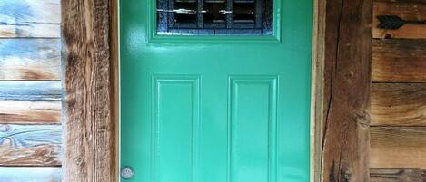 A turquoise door with a small window and the words "BIG HORN" above it, set in a rustic wooden cabin.