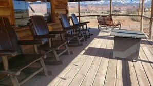 Eine Holzterrasse mit Adirondack-Stühlen und einem Korbstuhl-Tisch, mit Blick auf eine gebirgige Landschaft.