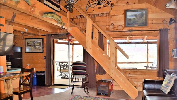 Ein rustikales Blockhaus-Interieur mit einer Holztreppe, einem Essbereich, einem Wohnzimmer mit Sofa und einem Kamin.