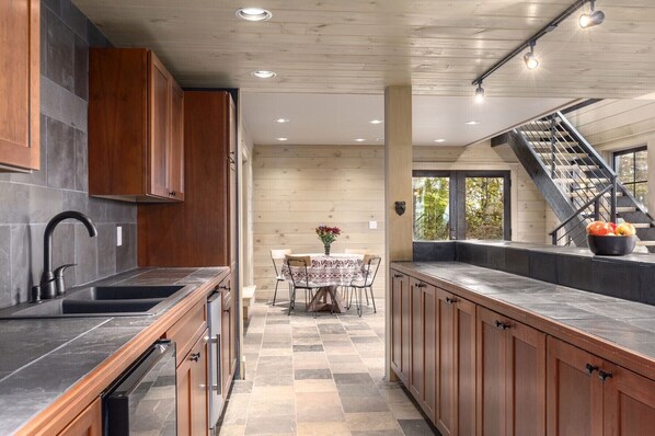 A modern kitchen with wooden cabinets, a black countertop, and a dining area with a table and chairs.