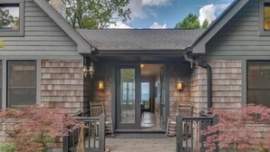 A two-story house with a covered porch, wooden siding, and a view into the interior. - Modern Home with Mountain Views, Hot tub, Pool Table, and Gourmet Kitchen. (Tryon)