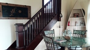 Ein Essbereich mit Glastisch und Metallstühlen, eine Holztreppe und ein Regal mit Dekoration.