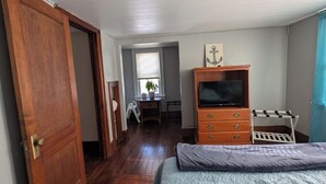 Ein Schlafzimmer mit Holztür, einem Bett mit Steppdecke, einem Schminktisch, einem Fernseher und einem Schreibtisch mit Stuhl.
