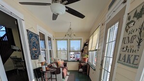 A cozy room with a ceiling fan, a window with a decorative wheel, a couch, and a sign that says 'go jump in the lake'. - 4-bedroom a short drive to the beaches, fishing, boat, jet express to Put In Bay (Port Clinton)