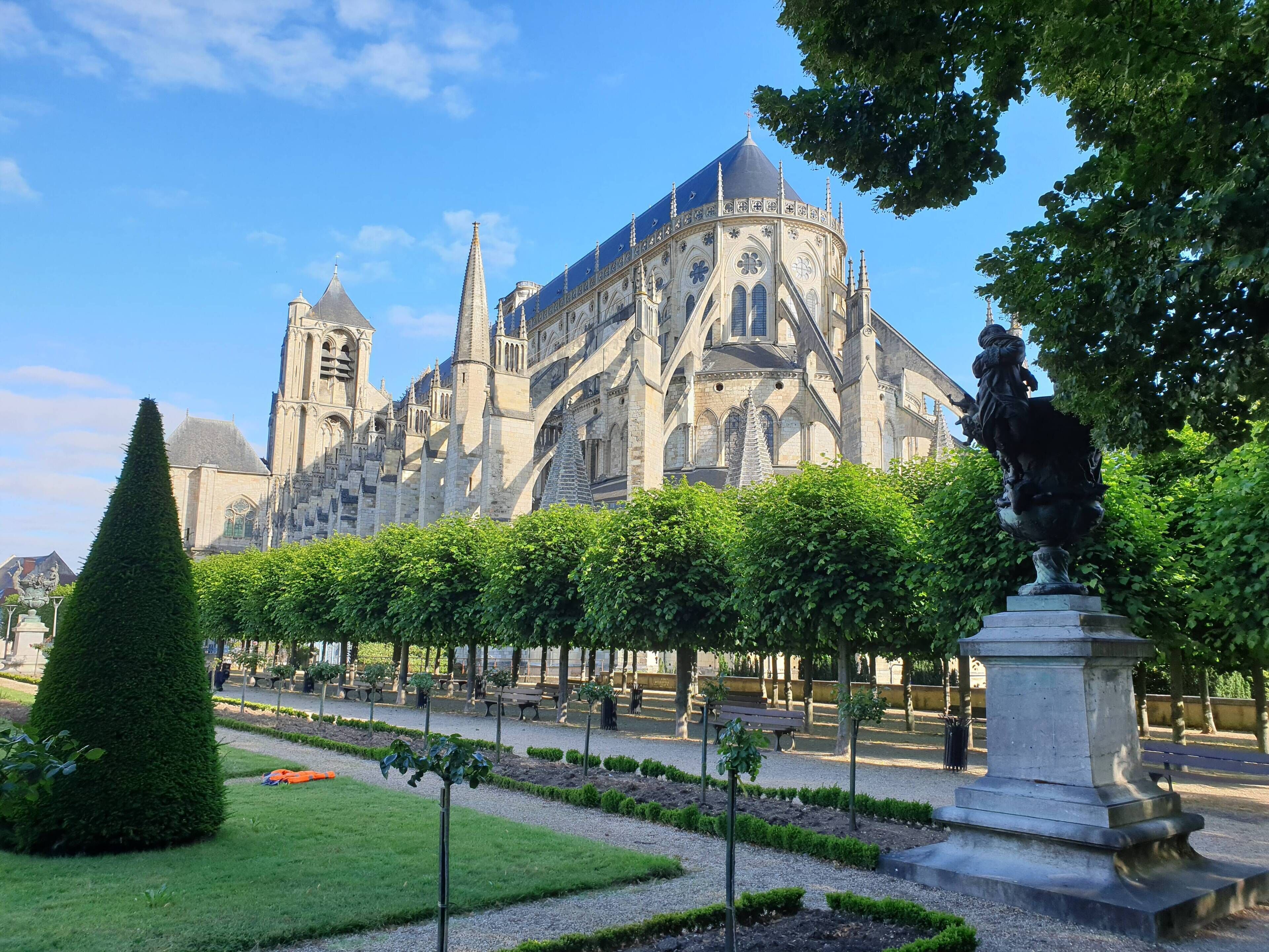Una catedral histórica con arquitectura intrincada, rodeada de un jardín bien cuidado con setos recortados y una estatua.